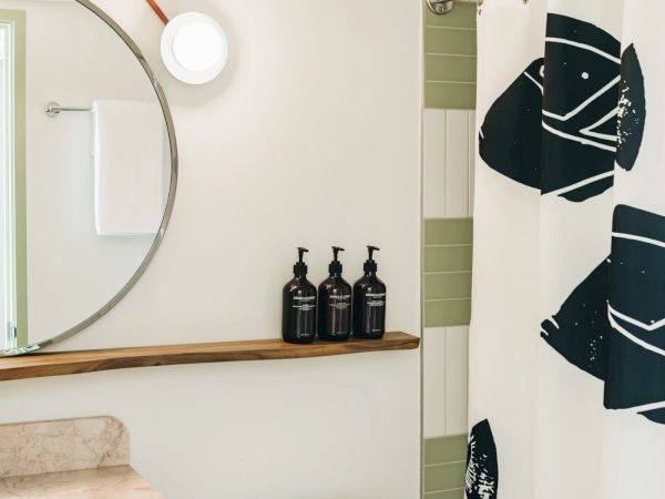 A bathroom with a round mirror, a sink, three black bottles, a white towel, and a shower curtain with black patterns is shown.