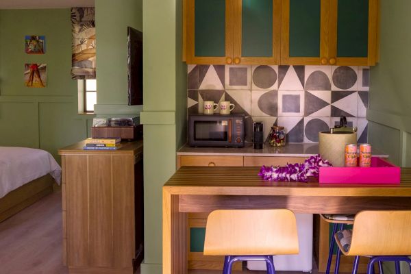 This image shows a cozy kitchen with a microwave, cupboards, and a table setup. There's an adjoining bedroom visible on the left side of the photo.