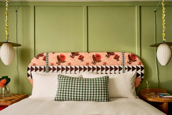 A neatly made bed with floral headboard, checkered pillow, and white pillows; flanked by pendant lights and nightstands with decor and flowers.