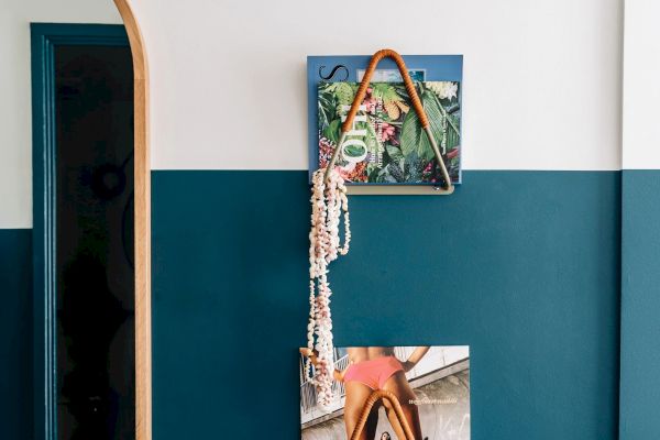 A wall display featuring a framed abstract picture, a triangular rope decoration, a string of seashells, and a partial image of a person on a beach.