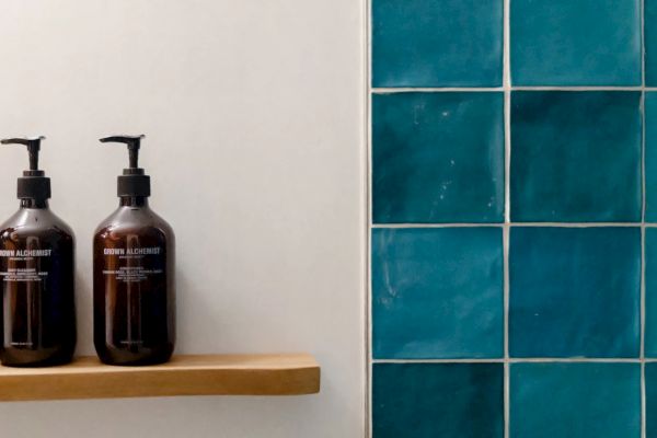 The image shows two pump bottles on a wooden shelf next to a wall with turquoise tiles.