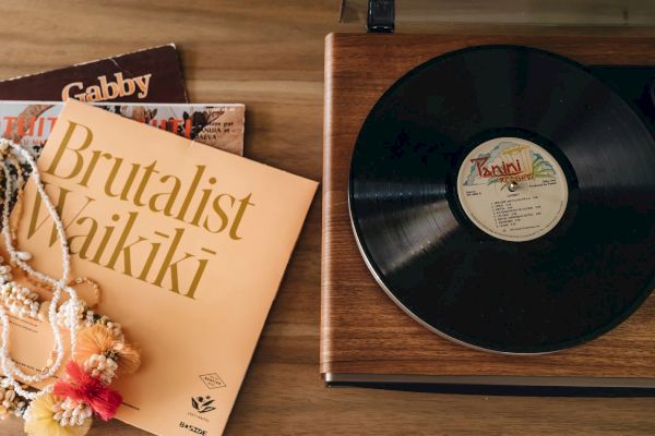 A vinyl record is on a wooden turntable, next to an album cover titled 