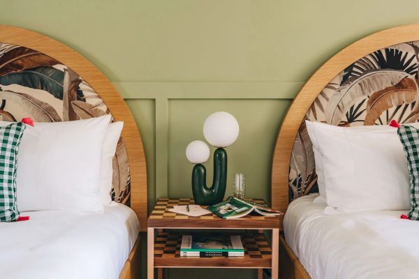 The image shows a cozy bedroom with two single beds, a green cactus-shaped lamp on a nightstand between them, and patterned headboards.