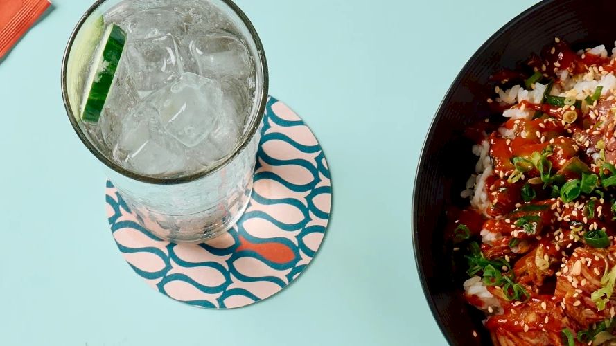 The image shows a bowl of food with rice and vegetables, a glass of iced drink with a slice of lime, and chopsticks placed beside the drink.