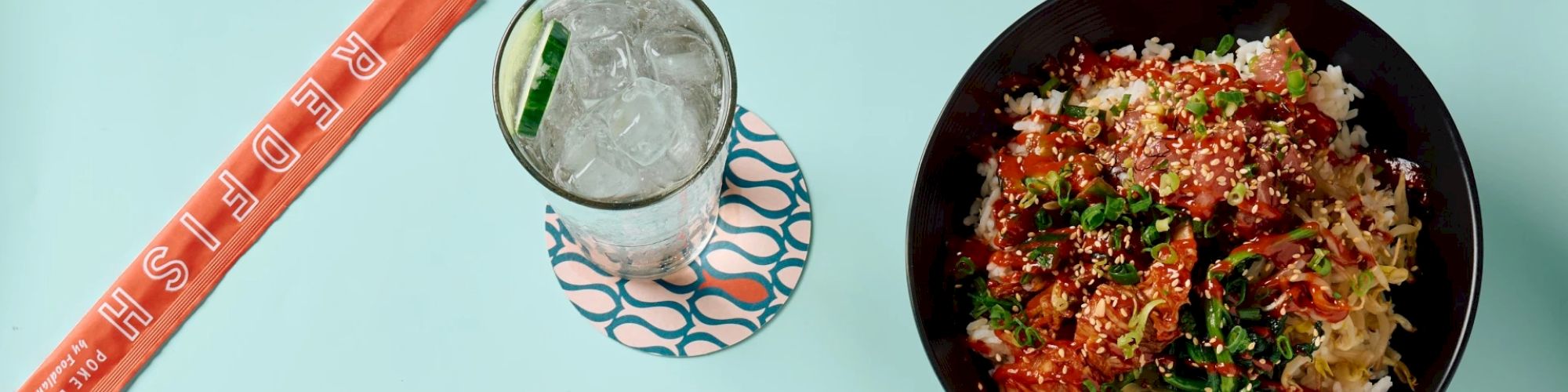 The image shows a bowl of food with rice and vegetables, a glass of iced drink with a slice of lime, and chopsticks placed beside the drink.