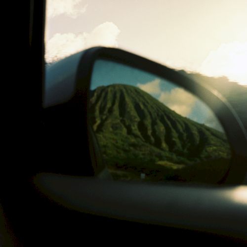 Une vue floue des montagnes &agrave; travers des vitres teint&eacute;es, avec des collines verdoyantes, des nuages et la chaude lumi&egrave;re du coucher de soleil en arri&egrave;re-plan.