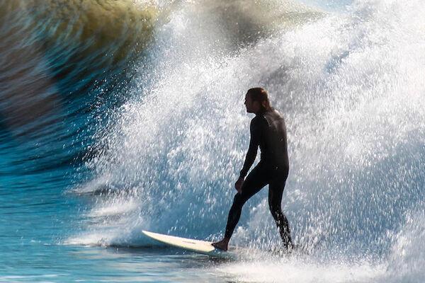 A surfer is riding a wave in the ocean while another person is submerged in the water with just their arm visible, creating a dynamic scene.