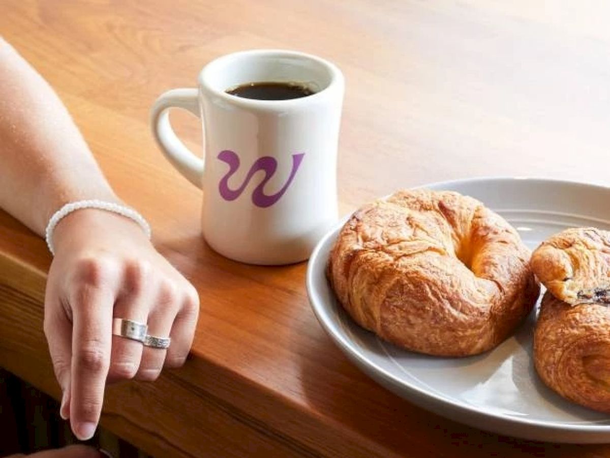 A person's hand rests on a wooden table next to a coffee mug with a 