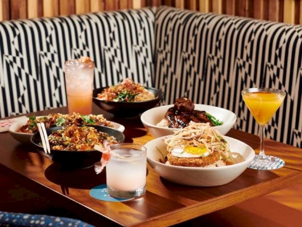 A table set with various dishes and drinks, including bowls of food and different beverages. The booth's upholstery has a geometric pattern.