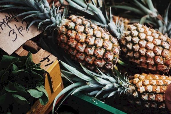 The image shows fresh pineapples for sale at a market, labeled at a price of 3 for 1. Also, there's a box of leafy greens in the corner.