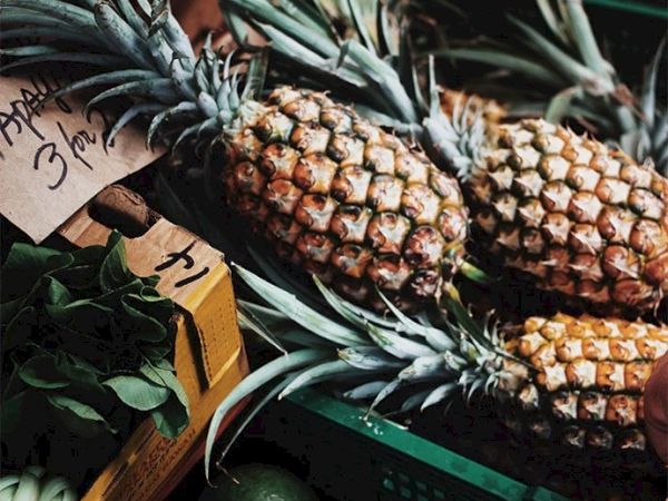 The image shows fresh pineapples for sale at a market, labeled at a price of 3 for 1. Also, there's a box of leafy greens in the corner.