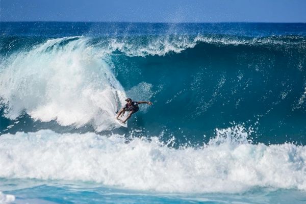 A surfer is riding a large wave in the ocean, with white foam forming at the crest and base of the wave, showcasing an impressive surf maneuvre.