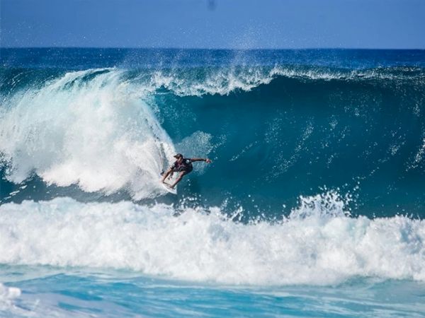 A surfer is riding a large wave in the ocean, with white foam forming at the crest and base of the wave, showcasing an impressive surf maneuvre.