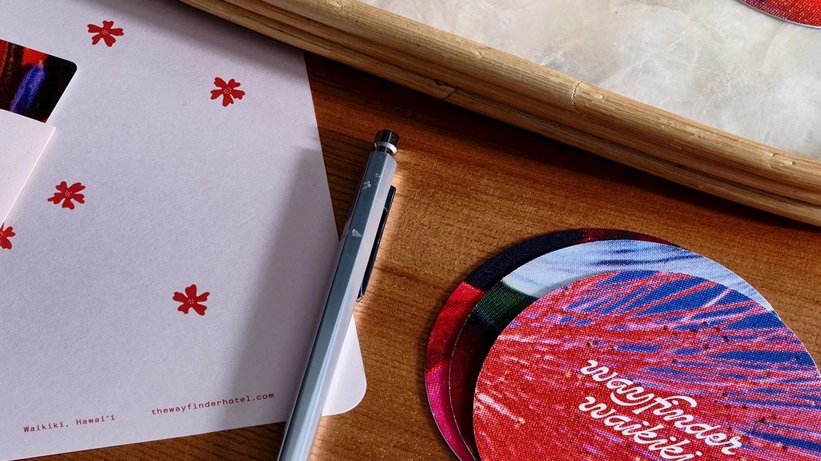 A minimalistic card reading "Stop and Smell the Flowers," a pen, circular colorful coasters, and an envelope on a wooden table.