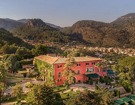 A vibrant building surrounded by lush greenery, nestled in a picturesque valley with mountains and a small village in the background.