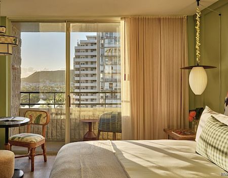 The image shows a cozy hotel room with a double bed, mountain view from a balcony, and stylish decor, featuring a table, chairs, and various light fixtures.