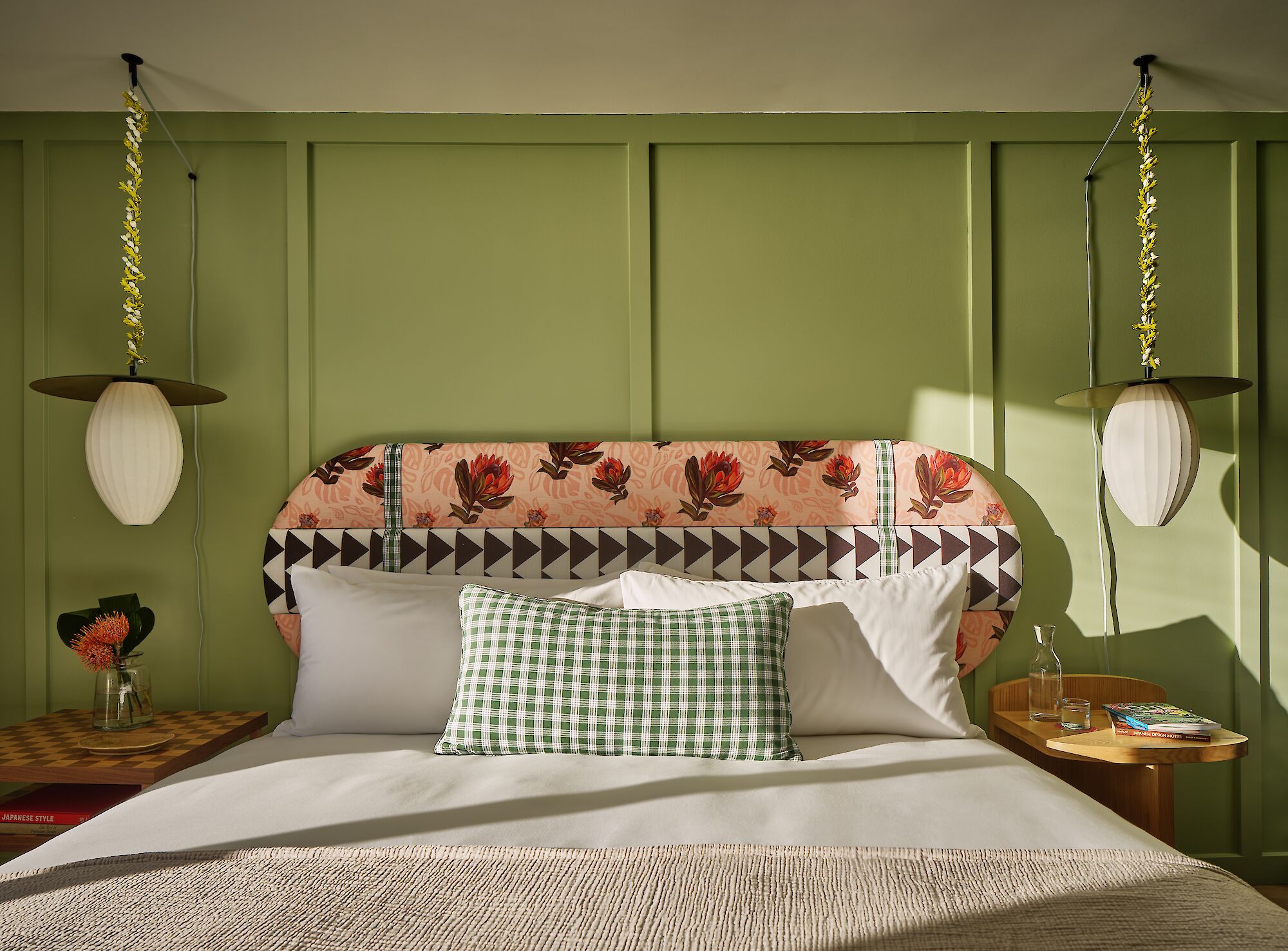 A stylish bedroom with a patterned headboard, hanging lamps, and a green wall.