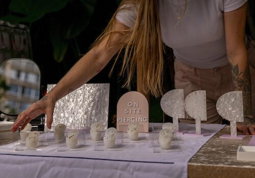 A person arranges items on a table, including ear models for piercings and a sign that says 