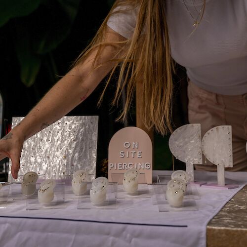 A person arranges items on a table, including ear models for piercings and a sign that says 