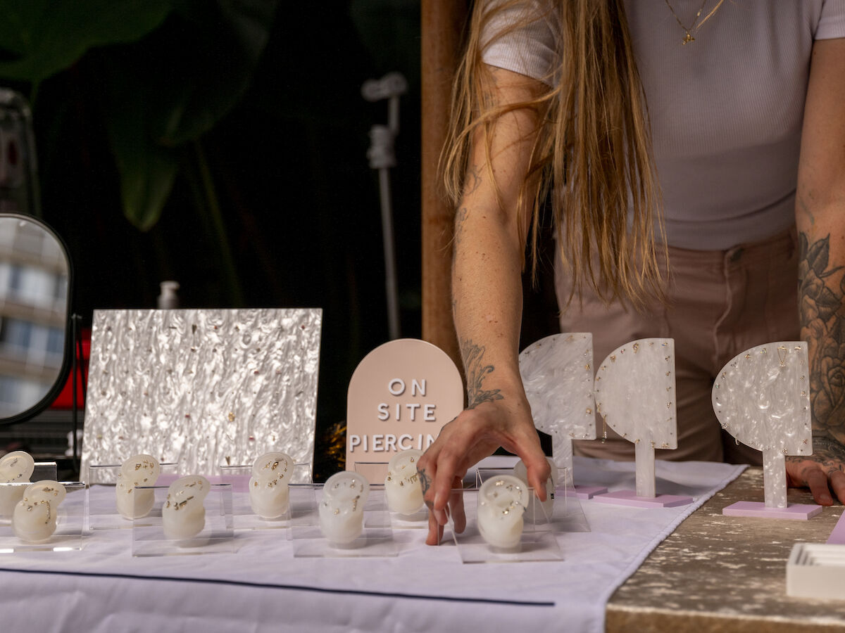 A person with tattoos sets up a display of earring stands, jewelry, and a sign that says 