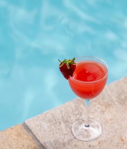 プールの端に置かれた、縁にイチゴが飾られた赤い飲み物のグラス。