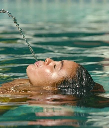 人が頭を後ろに傾け、口から水を噴き出しながらプールに浮かんでいる。