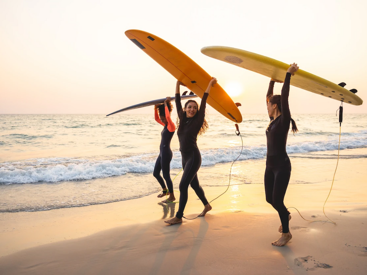 Three people walking on a beach, carrying surfboards over their heads, with the ocean and sunset in the background.