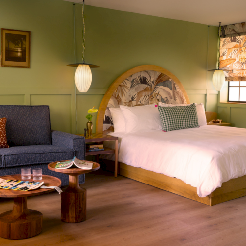 Cozy bedroom with a wooden bed, patterned canopy, blue sofa, coffee tables, and warm hanging lamps.