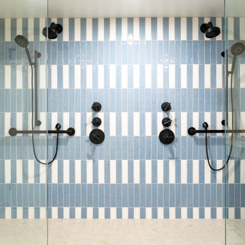 A shower with blue and white striped tiles, two showerheads, and black fixtures. Glass doors enclose the space.