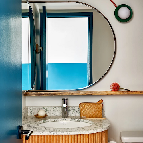 A modern bathroom with a round mirror, wooden vanity, window, and wall decor featuring three circular frames connected by red lines.