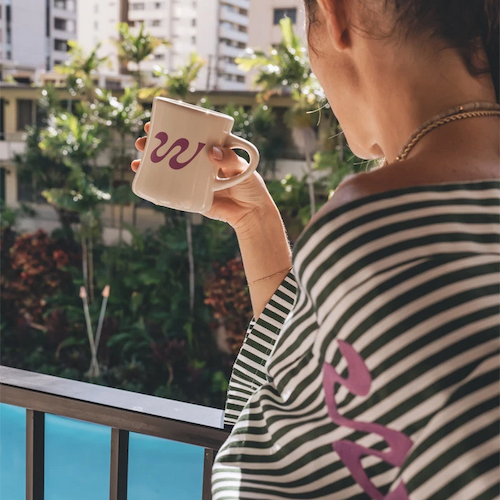 A person is standing on a balcony, holding a mug with the letter 