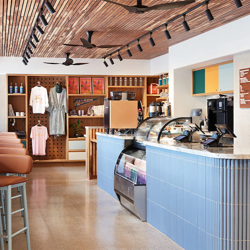 A modern café with a counter display, bar stools, ceiling fans, and a retail area showcasing clothing and other items on shelves.