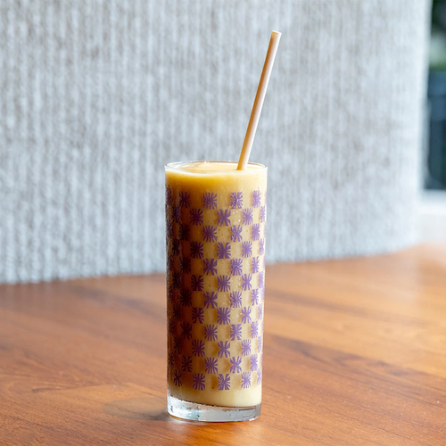 This image shows a tall glass with a checkered pattern containing an orange-colored beverage and a straw, placed on a wooden surface.