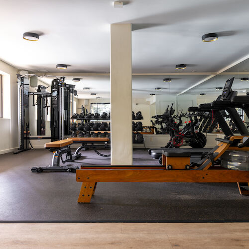 This image shows a gym with various exercise equipment including treadmills, weight machines, and benches, with mirrors on the wall.