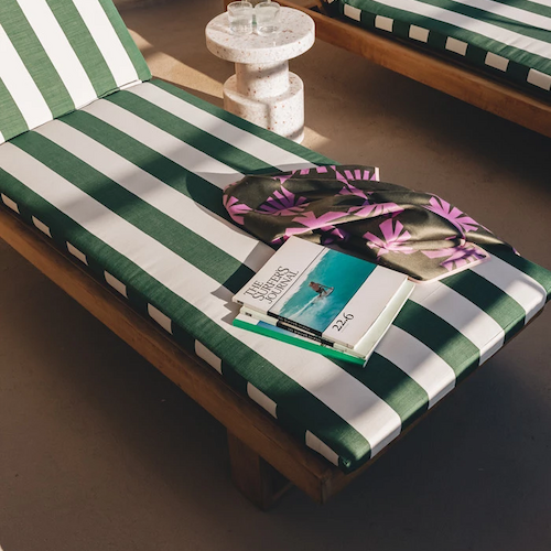 Two green and white striped lounge chairs, a small round table with a glass, and magazines and sunglasses placed on one of the chairs.