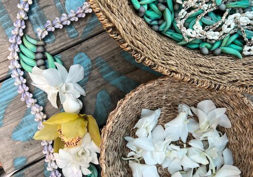 The image shows two wicker baskets with turquoise and white beads, and a floral necklace made of white, yellow, and green flowers and beads.