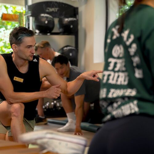 A group of people are exercising indoors, with one individual seemingly instructing or guiding others in the workout session.