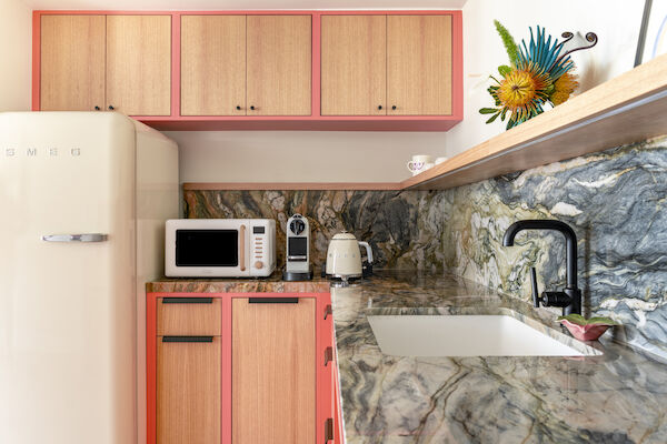 A stylish kitchen features pink accents, a marbled countertop, a sink, a SMEG fridge, microwave, coffee maker, kettle, and vibrant flower decor.