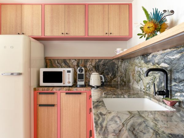A stylish kitchen features pink accents, a marbled countertop, a sink, a SMEG fridge, microwave, coffee maker, kettle, and vibrant flower decor.
