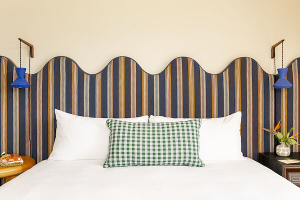 The image features a bed with white pillows, a green checkered cushion, a colorful wavy headboard, and blue bedside lamps.