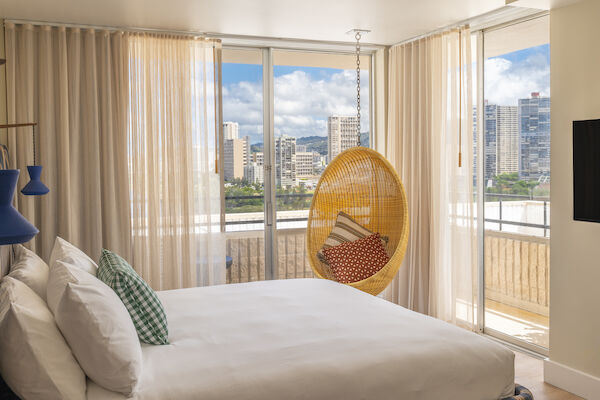 A modern bedroom with a large bed, hanging chair, and floor-to-ceiling windows showing a cityscape view, with sheer curtains partially drawn.