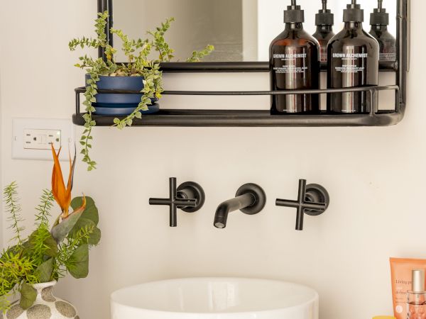 A bathroom counter with a white vessel sink, plants, soap dispensers, and a mirror with a shelf holding more bottles and a small plant ends the sentence.