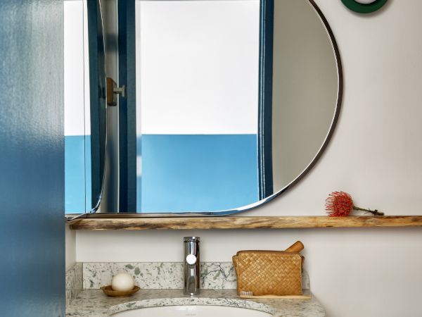 A stylish bathroom vanity with a round mirror, wall bulbs, sink faucet, and toiletries on the countertop.