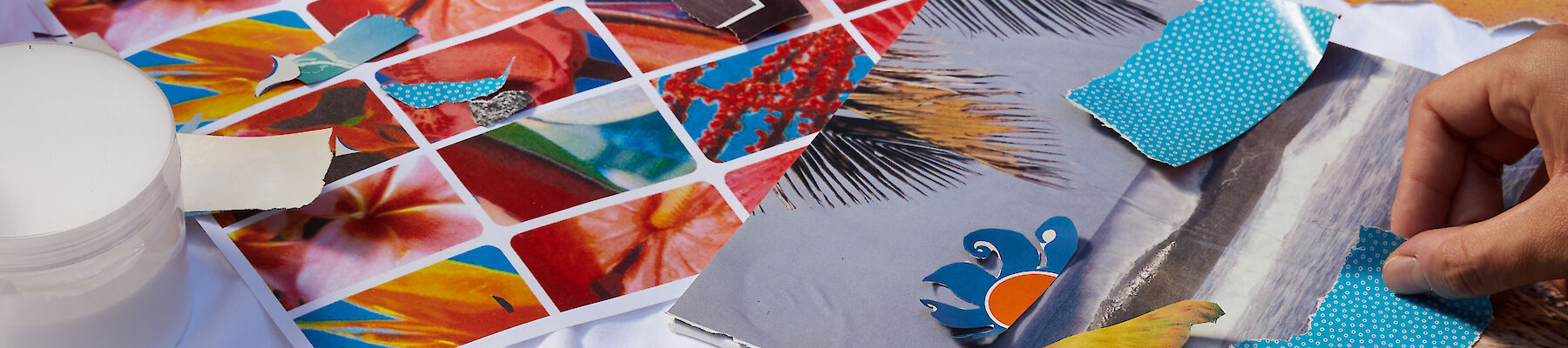 Three people working on a collage with various materials, such as magazines, paper, scissors, and glue, on a table.