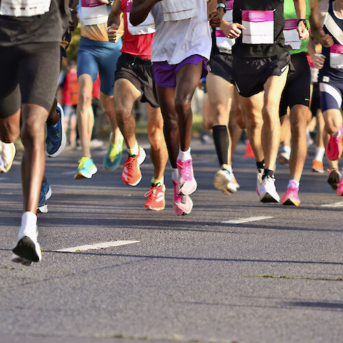 A group of runners participating in a race, seen from the legs down, with colorful running shoes and race bibs visible.