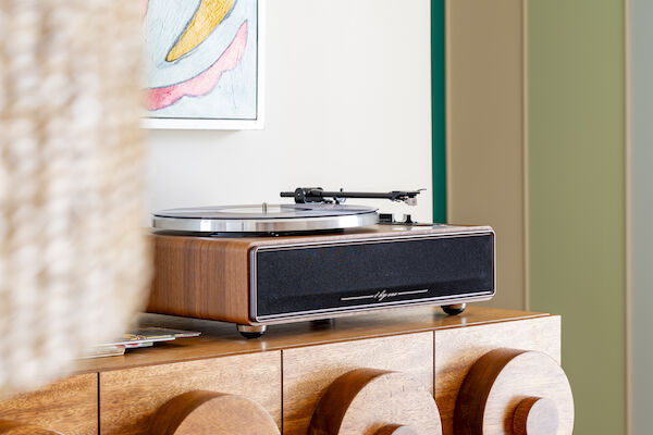 A modern vinyl record player sits atop a stylish wooden cabinet with circular patterns; a colorful abstract painting hangs above it.