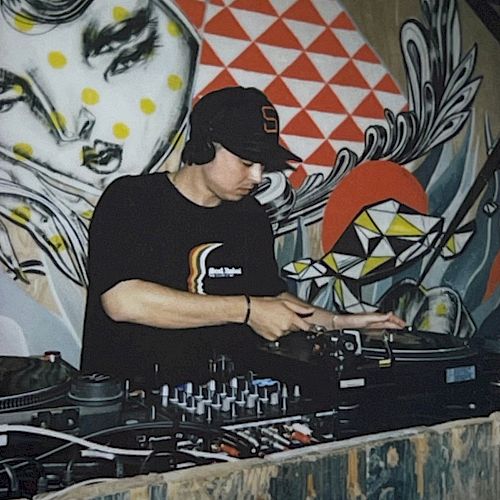 A DJ is mixing music on turntables in front of a colorful mural with abstract and geometric designs.