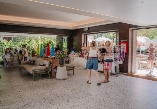 People are browsing a small indoor shop with colorful items on display, and others are outside in a sunny area.