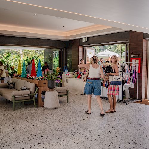 People are browsing a small indoor shop with colorful items on display, and others are outside in a sunny area.