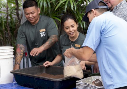 People are gathered around a table with containers, engaging in an activity involving a plastic bag and a tray.